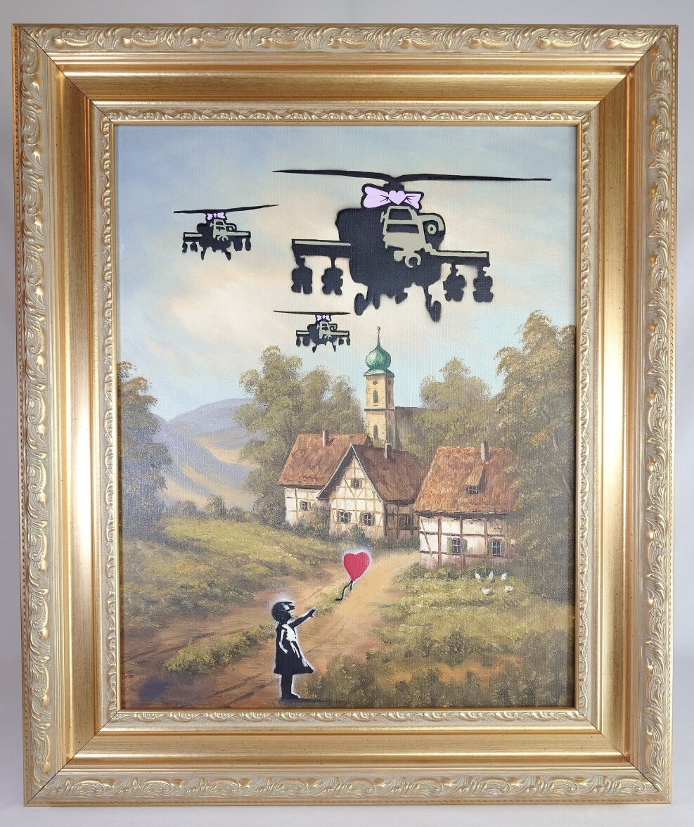 Peinture de Fictional World dans un cadre doré : un paysage de village ancien sur lequel sont peints des hélicoptères militaires noirs à nœuds roses et, au premier plan, une fillette tenant un ballon rouge en forme de cœur